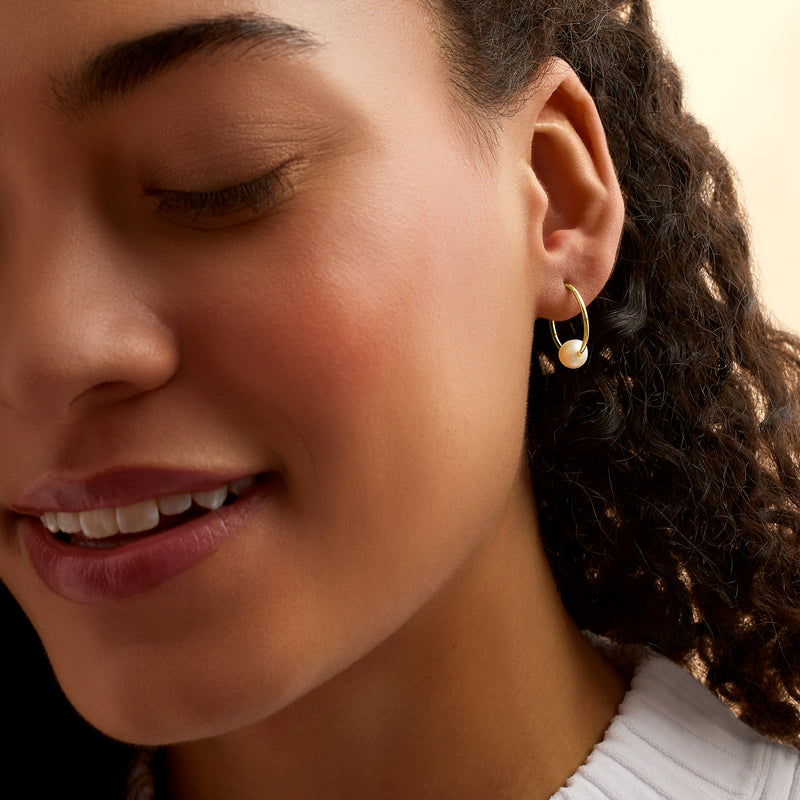 Yellow gold hoop earrings with white pearl charm on hinged hoops, worn