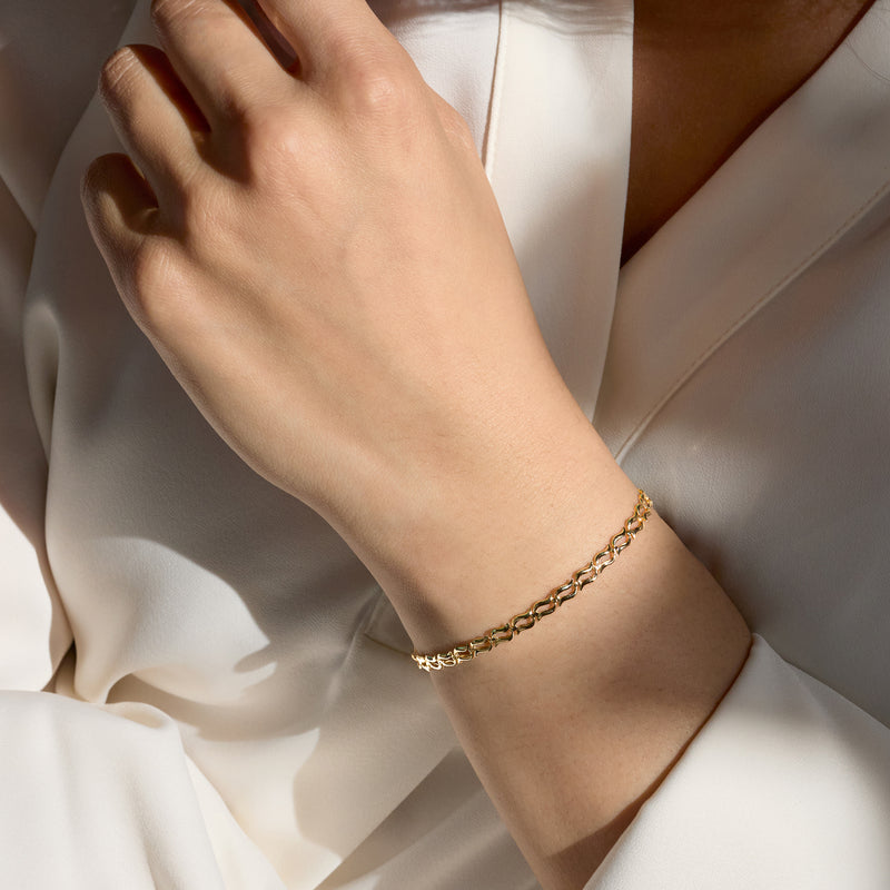 Wavy-link gold bracelet on wrist, clasp visible, polished yellow shine
