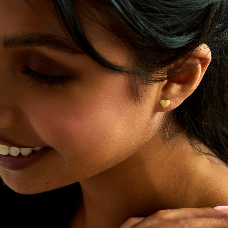 Yellow gold heart stud earrings on ear, small polished hearts
