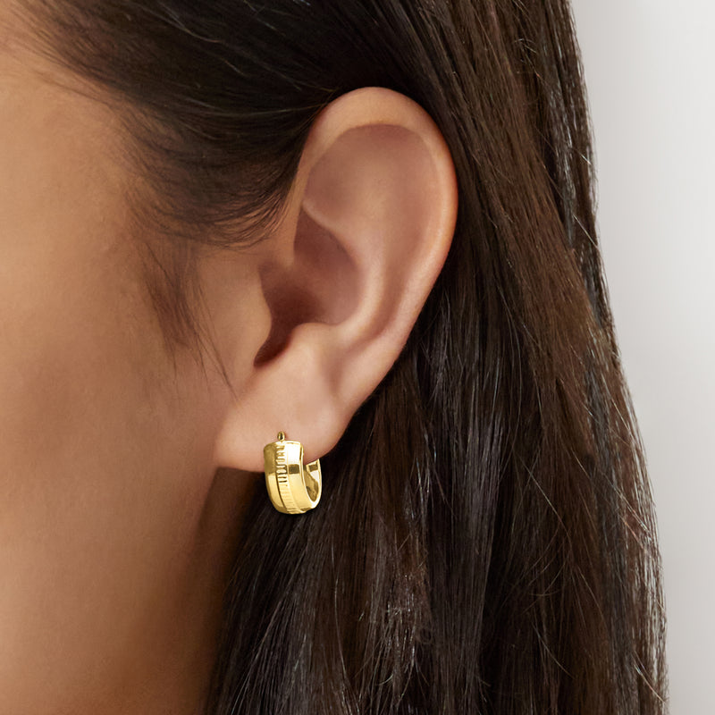 Yellow gold huggie hoop earrings on ear, small round hoop with ridged front