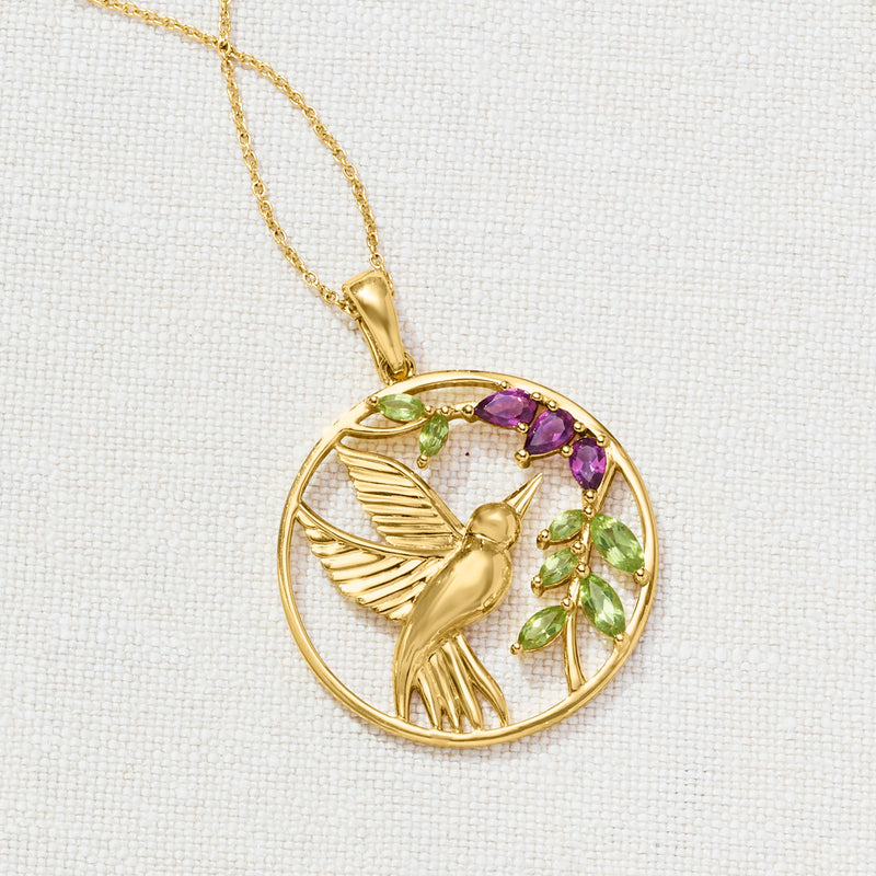 Close-up gold hummingbird pendant necklace with peridot and rhodolite gemstones in a round frame