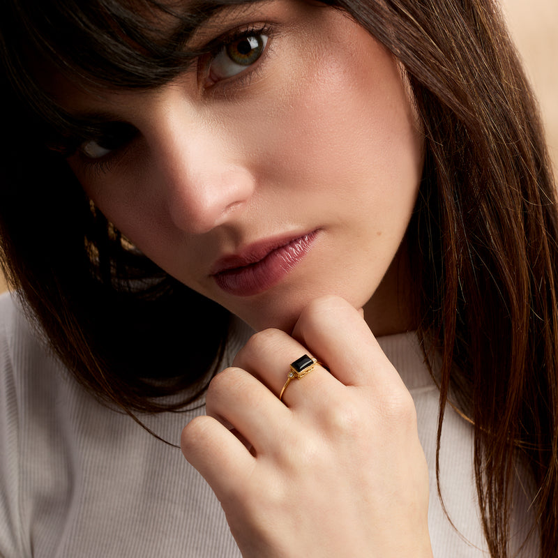 Gold ring on finger with rectangular black onyx centerpiece and diamond side details