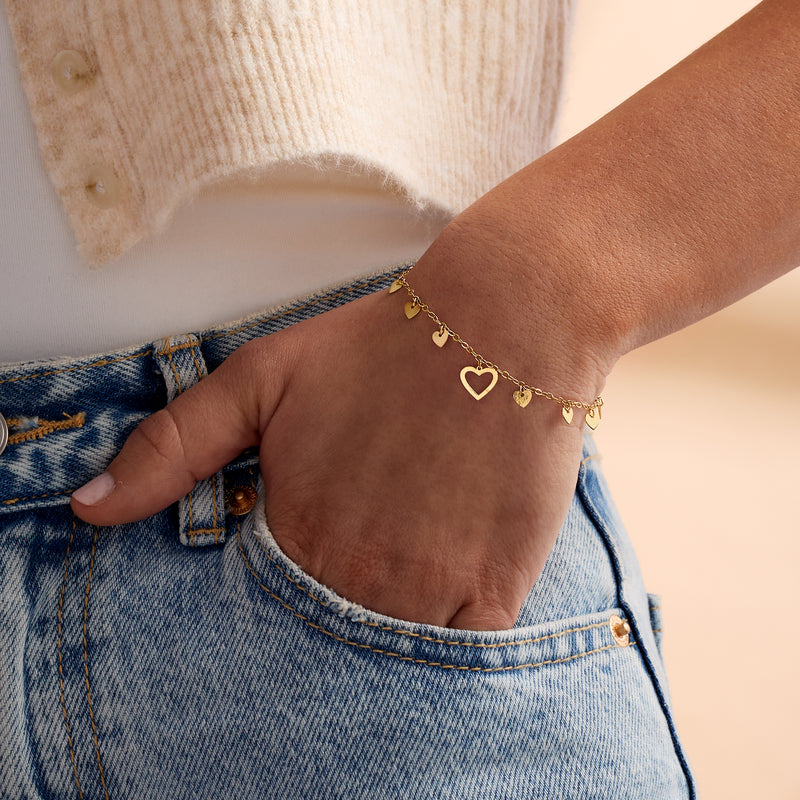 Worn on wrist: yellow gold heart station bracelet with small dangling heart charms
