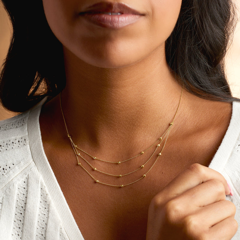 Three-strand yellow gold bead station necklace layered at the neck