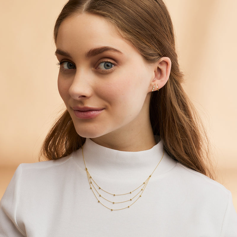 Layered yellow gold bead station necklace on model wearing a white top