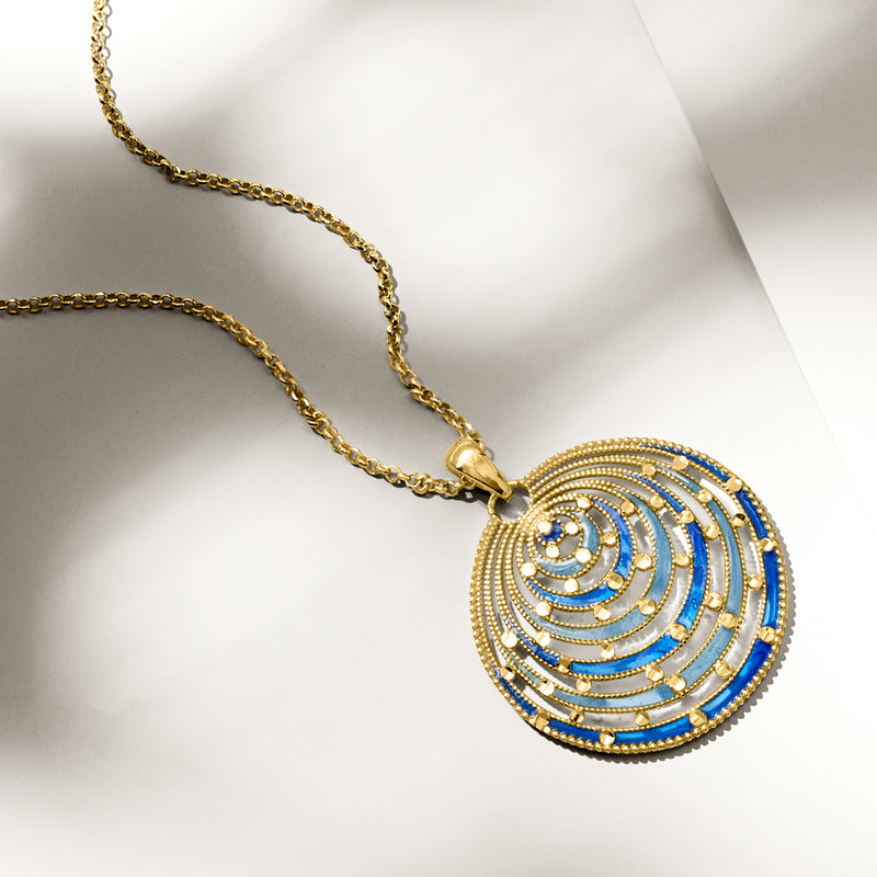Close-up of round blue enamel swirl pendant on gold-tone chain with bail.