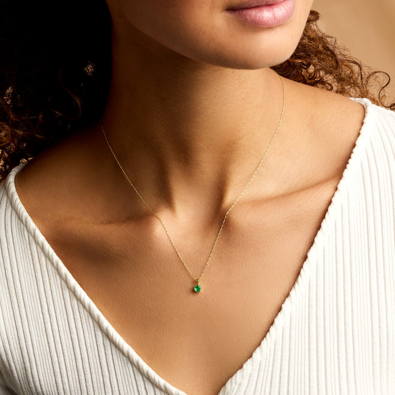 Emerald pendant necklace worn on 14kt yellow gold chain with round green gemstone