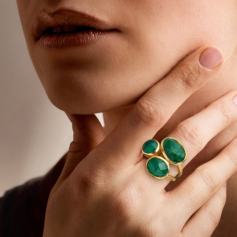 Three-stone emerald ring on finger, oval green gemstones in gold bezels