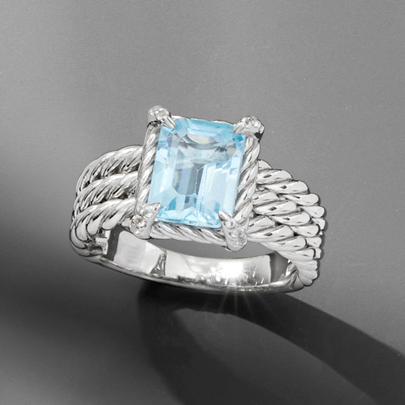 Sky-blue topaz engagement-style ring with emerald-cut center stone in twisted halo