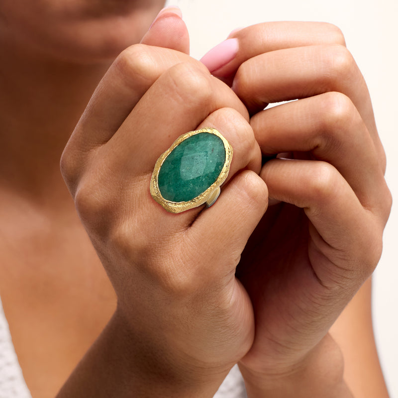 Gold oval emerald-green ring on hand, bezel-set gemstone in hammered gold band