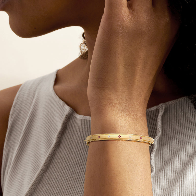Gold bangle on wrist with red and blue flower accents and small sparkle stones.