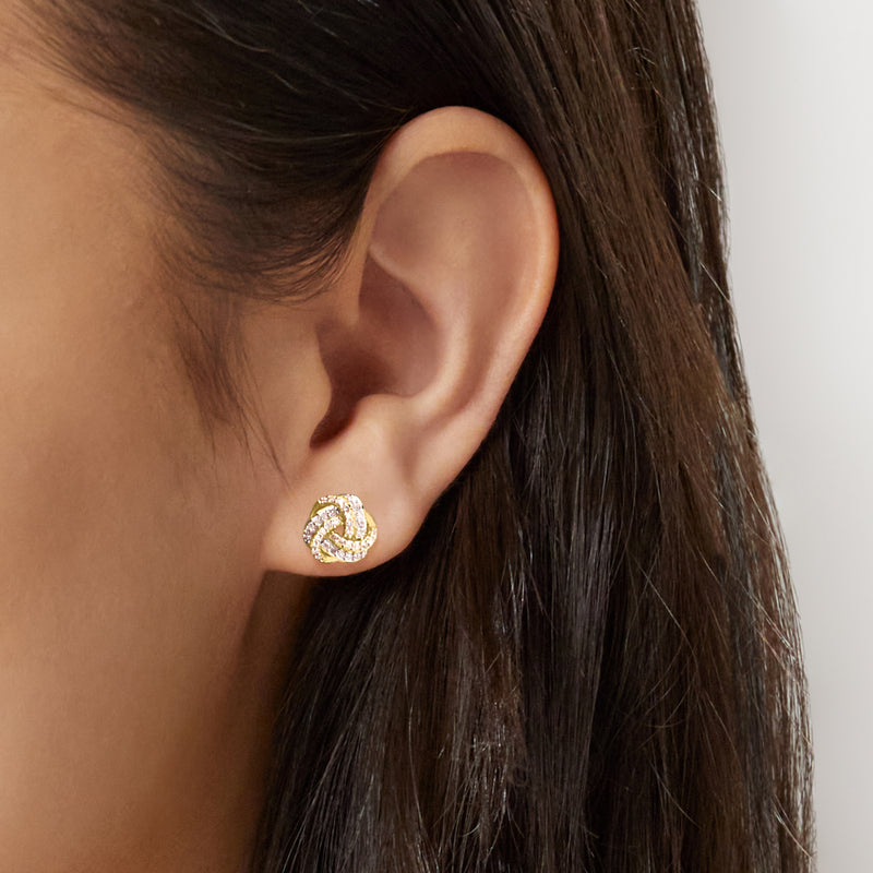 Diamond love knot stud earring worn on ear in two-tone gold with clear stones