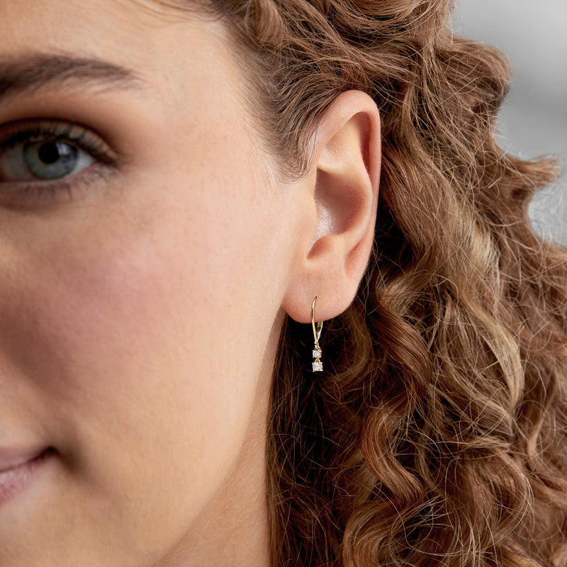 Diamond drop leverback earrings with three round stones worn on model's ear