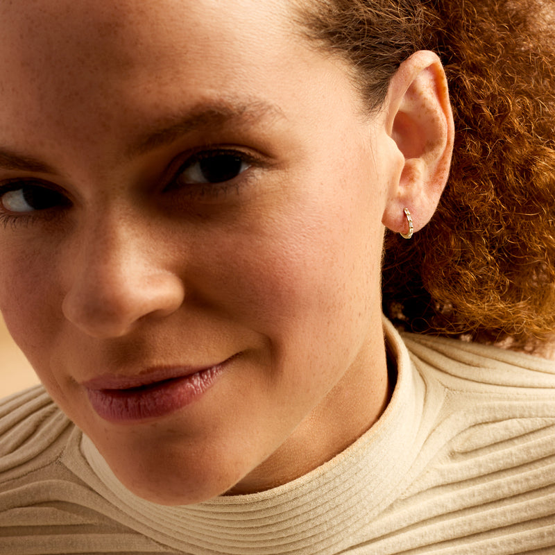 Gold huggie hoop earrings with diamond accents on ear