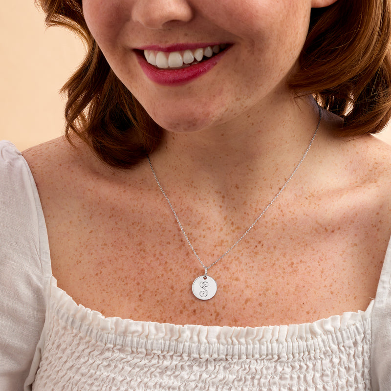 Sterling silver circular initial pendant necklace on a fine chain, worn by model