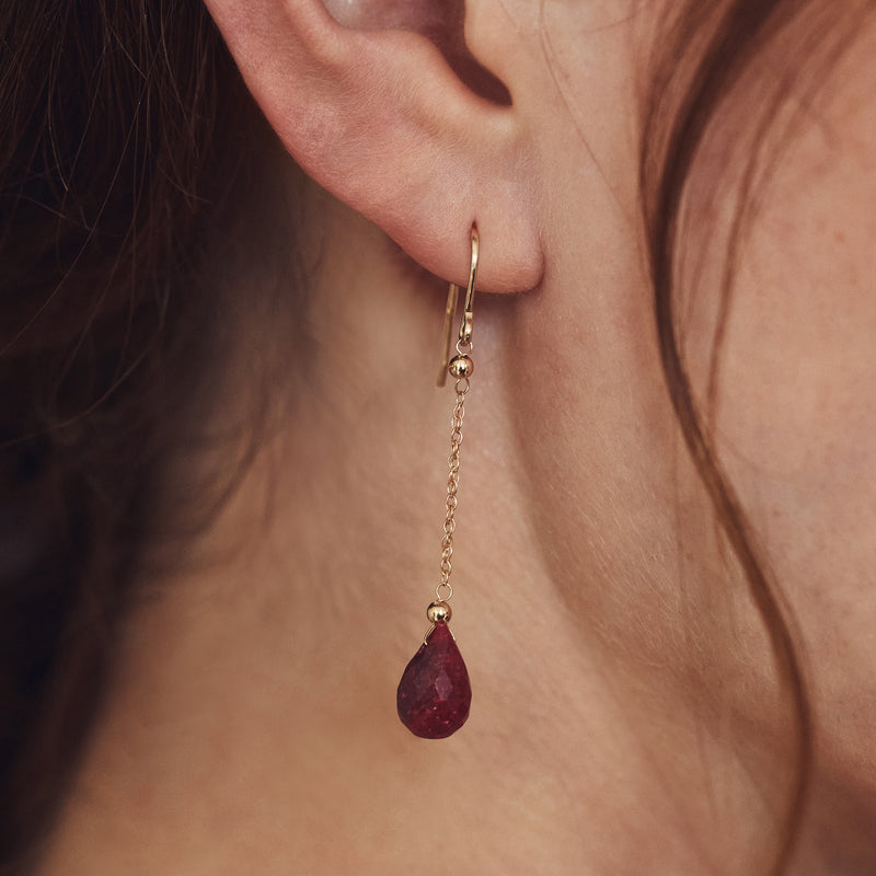 Gold earwire with dangling ruby teardrop charm, dark red stone