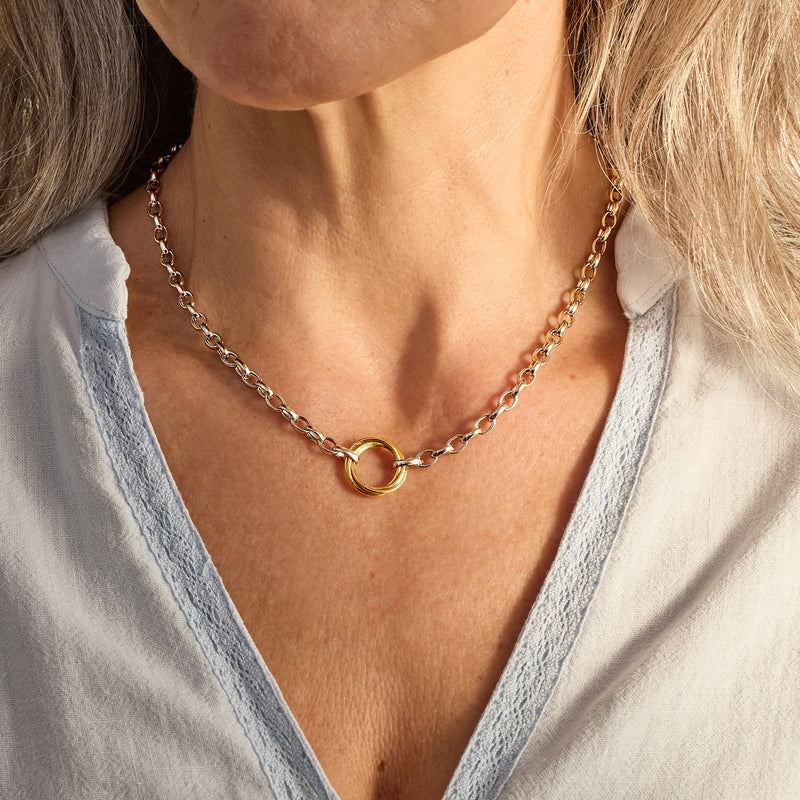 Necklace worn at collarbone: silver rolo links with gold multi-ring centerpiece.