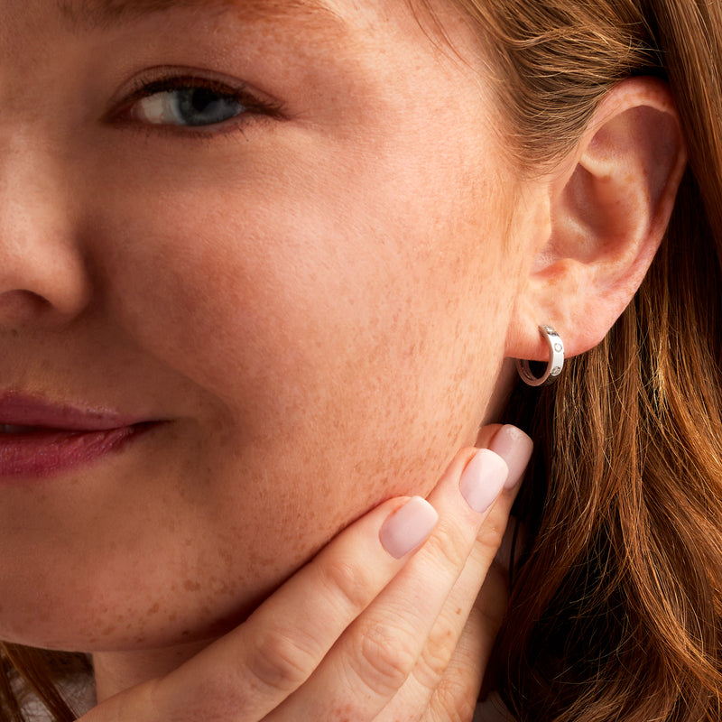 Huggie hoop earrings with round diamond accents worn on ear, close-up