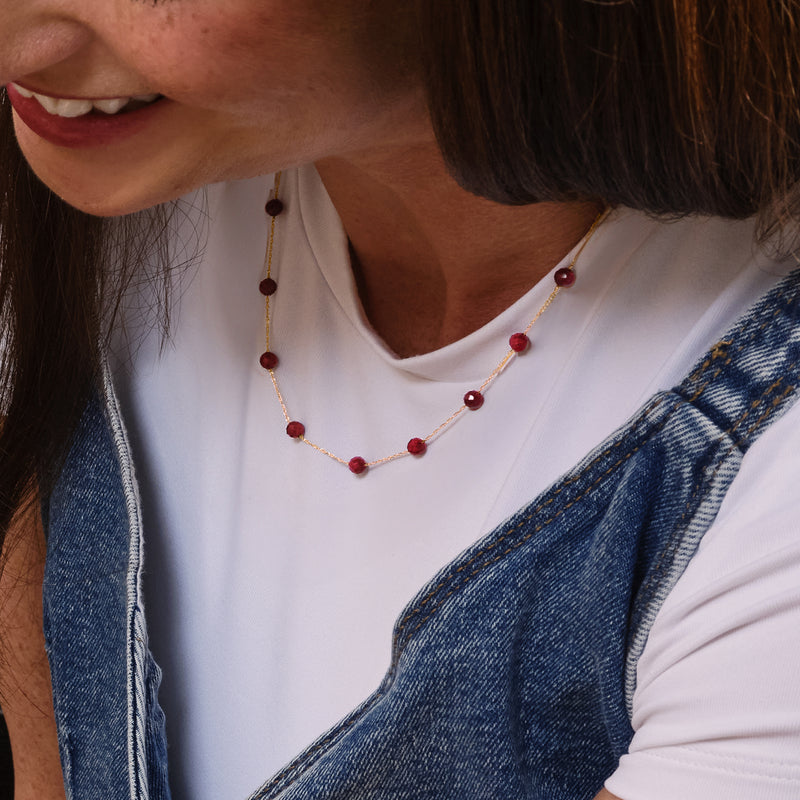 Ruby bead station necklace with 10kt yellow gold chain and round red beads on neck.