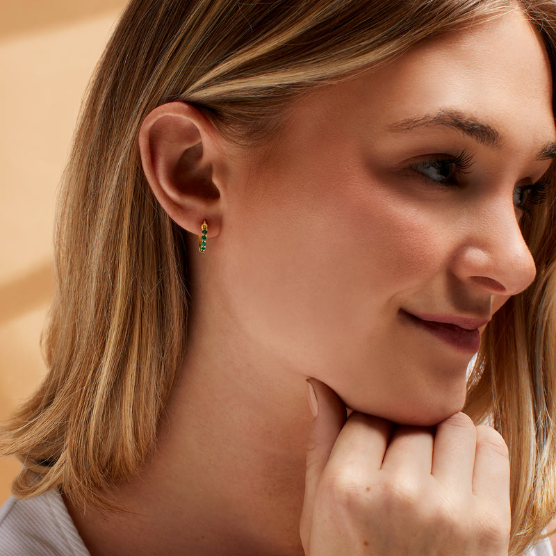 Emerald huggie hoop earrings in yellow gold worn on model ear
