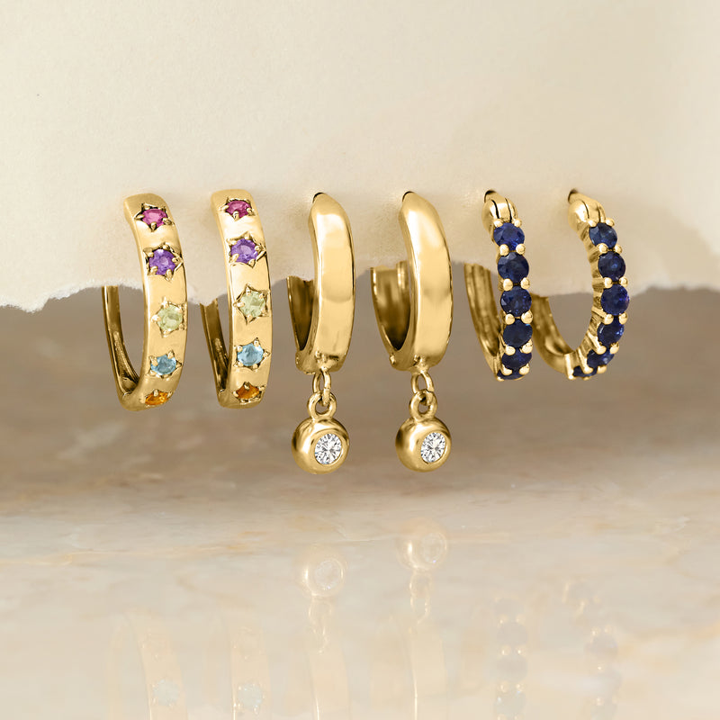 Yellow gold huggie hoop earrings with blue, pink, and green gemstone accents