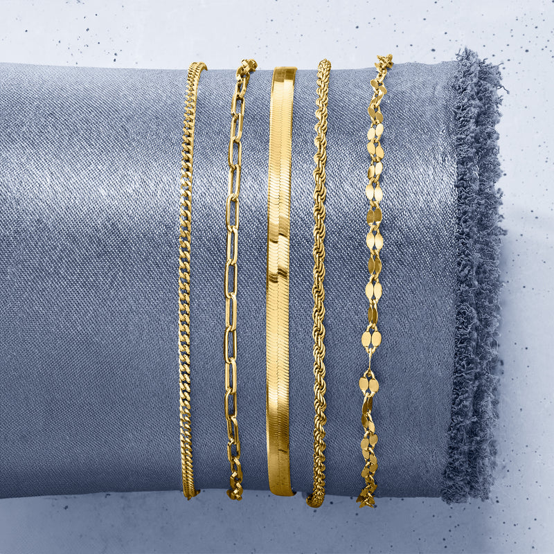 Five gold-tone bracelets stacked, showing different chain textures and clasps