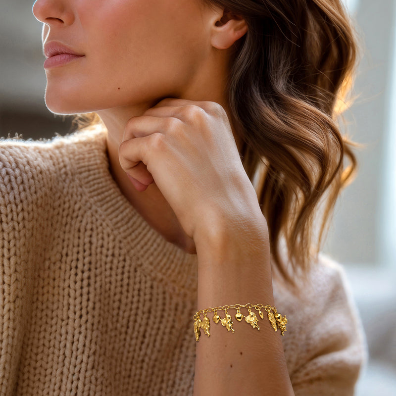 Gold-tone charm bracelet on wrist with cherub and heart charms