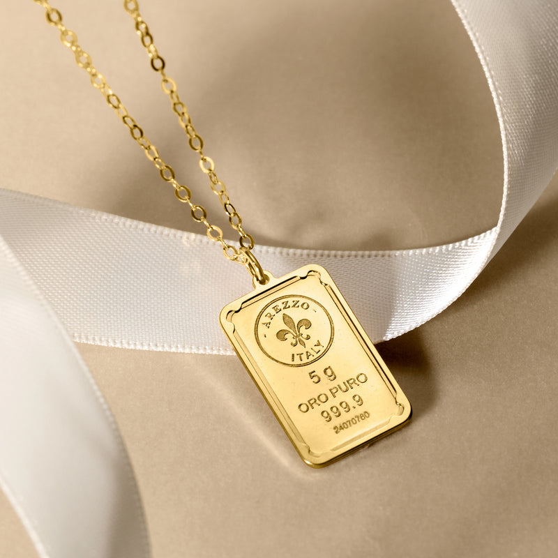 Close-up of gold rectangular ingot pendant on link chain with fleur-de-lis mark