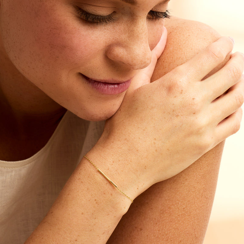 Yellow gold bar bracelet worn on wrist with thin chain and toggle clasp
