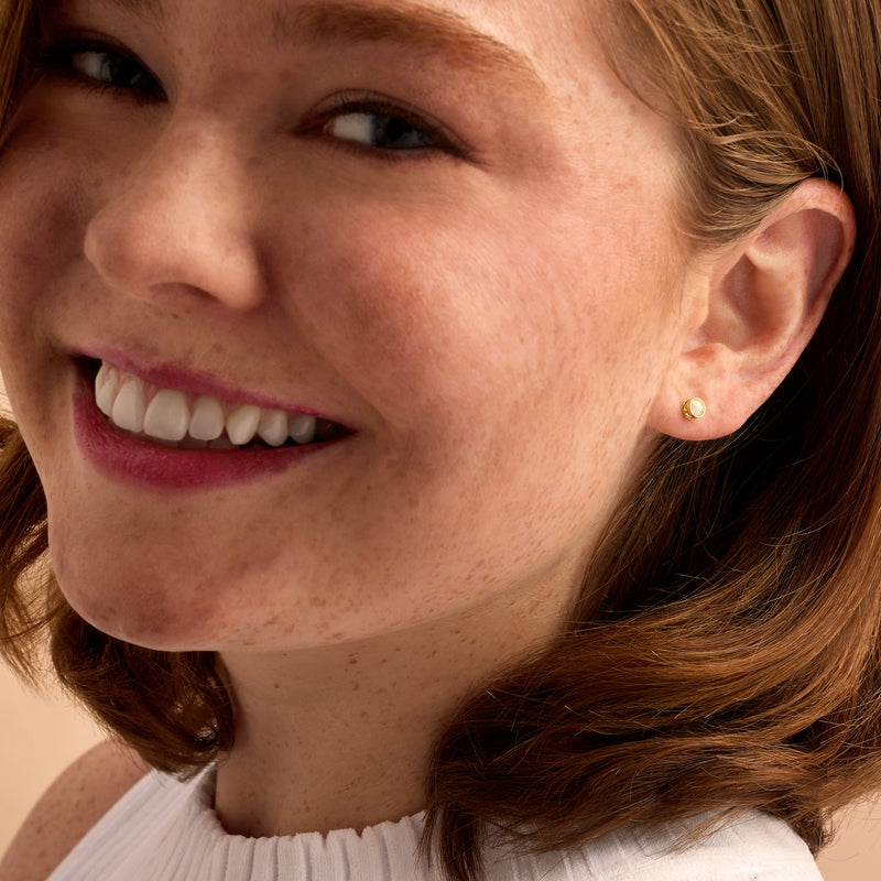 14kt yellow gold opal stud earrings on a model's ear, round iridescent stones