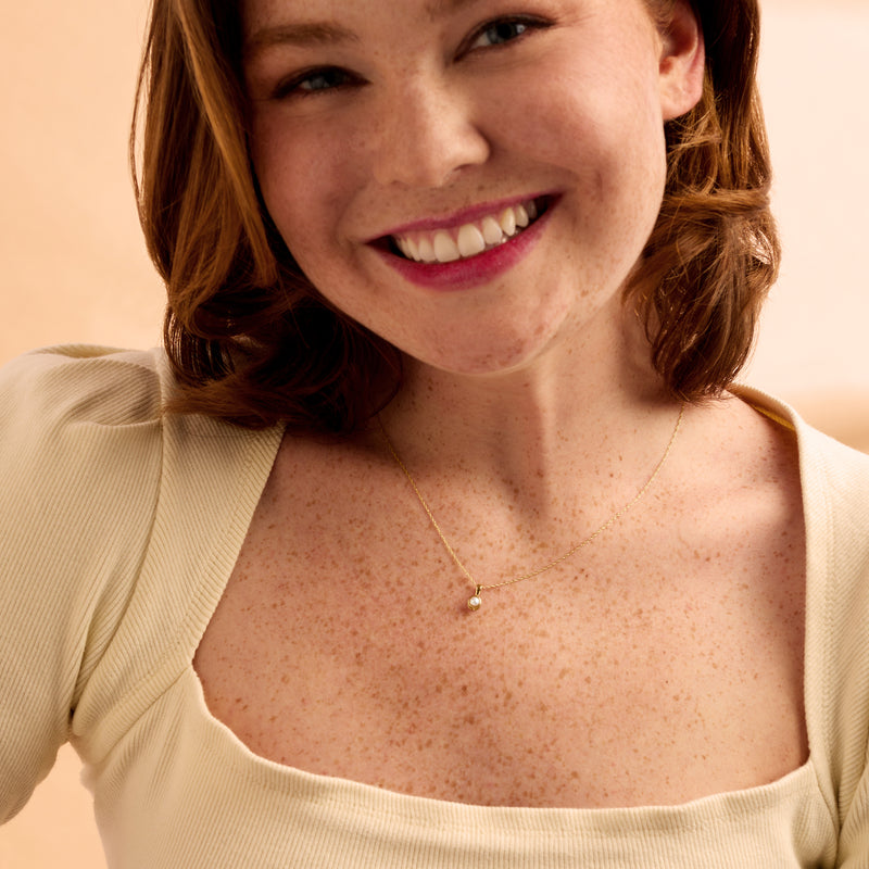 Yellow gold chain necklace with small round cultured pearl pendant on model