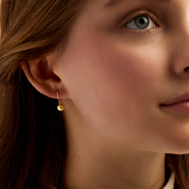 Gold ball drop earrings on ear, small spherical dangles with earwire