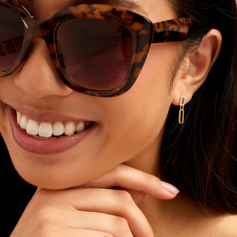 Gold diamond-accent drop earrings with linked oval design, worn on ear