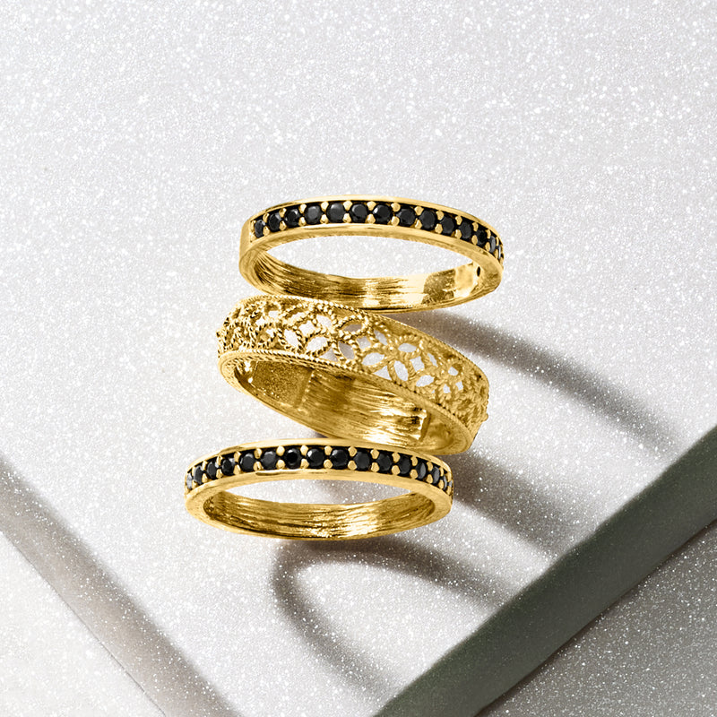 Three gold rings overlapping: black bezel band and filigree scrollwork accents
