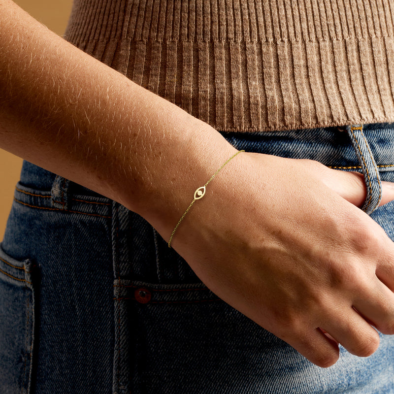 Yellow gold evil eye bracelet on wrist with small oval charm