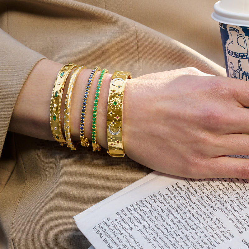 Wrist wearing a stack of five gold-tone bangles with blue and green star motifs