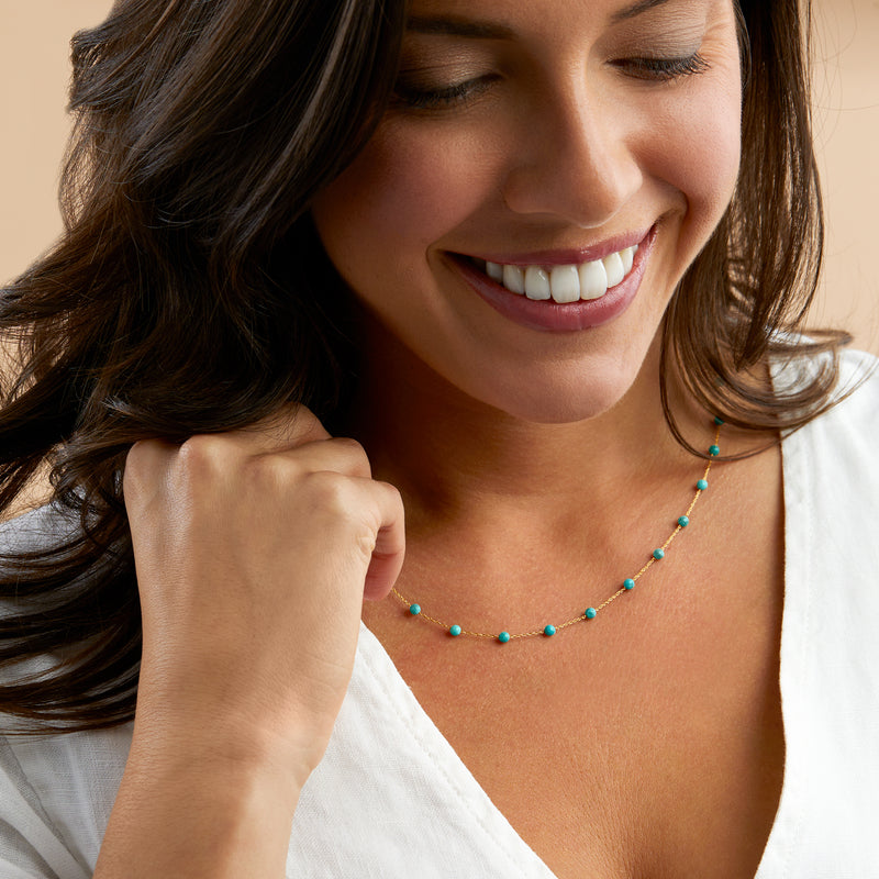 Woman wearing turquoise bead station necklace; 14kt yellow gold chain with round beads