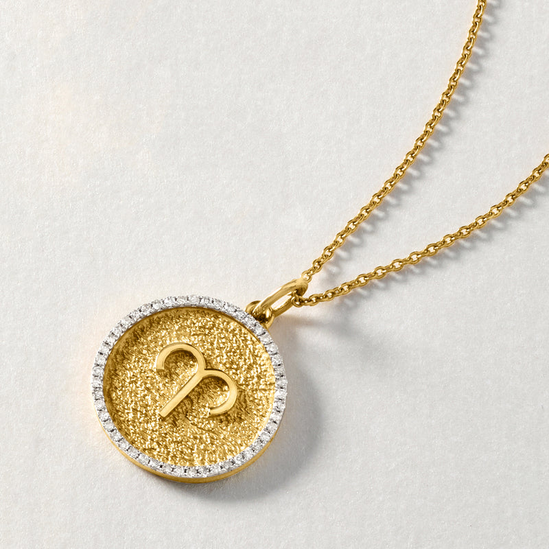 Close-up of gold-tone round zodiac pendant necklace with diamond-like border and engraved glyph