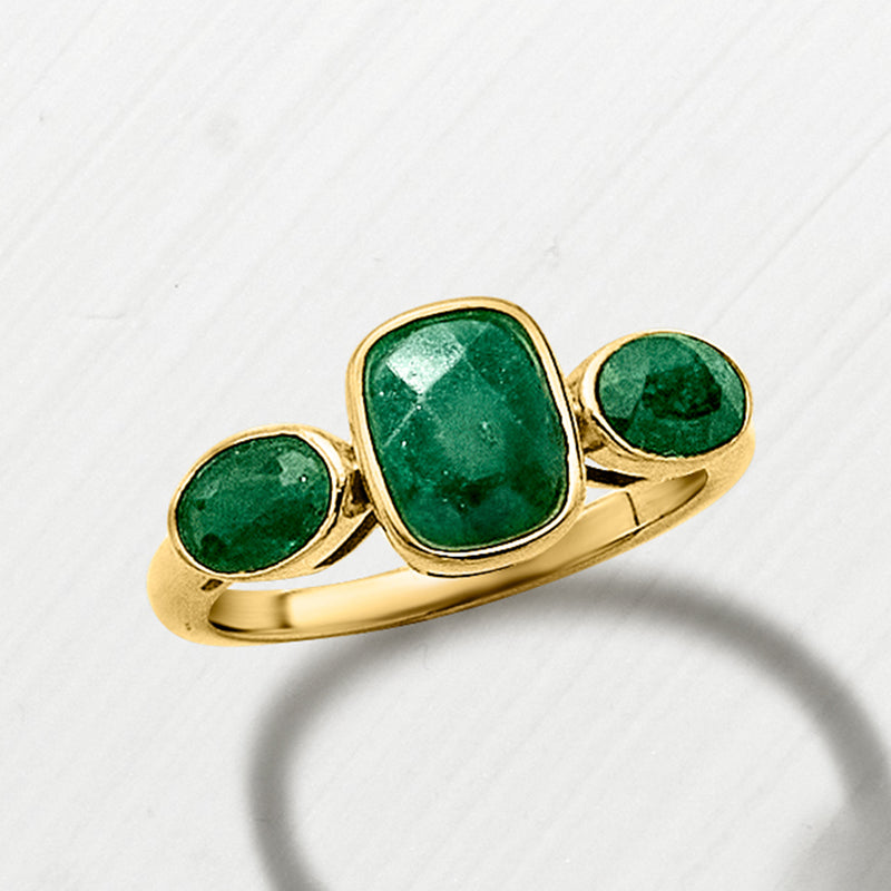 Gold three-stone ring featuring three green gemstone settings