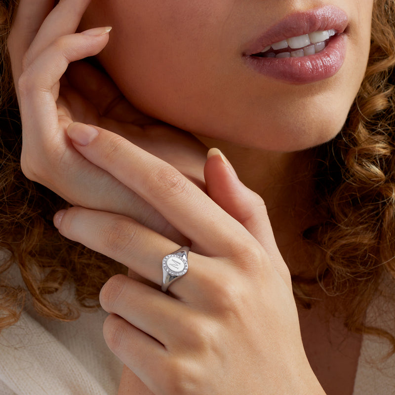 Sterling silver oval signet ring with diamond halo and monogram, worn close-up