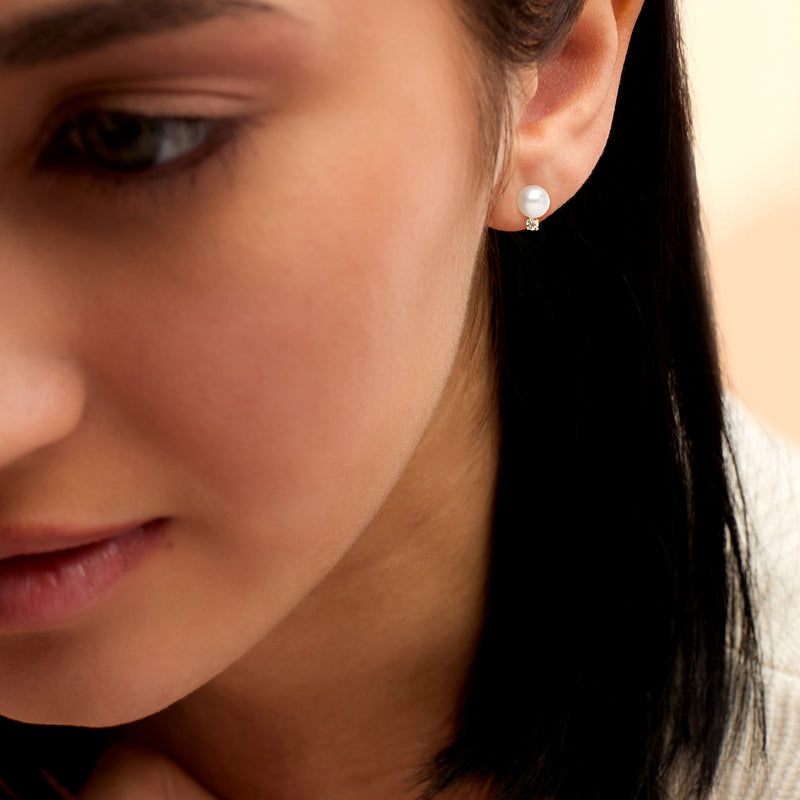 Cultured pearl stud earrings with diamond halos, shown on-ear with gold posts