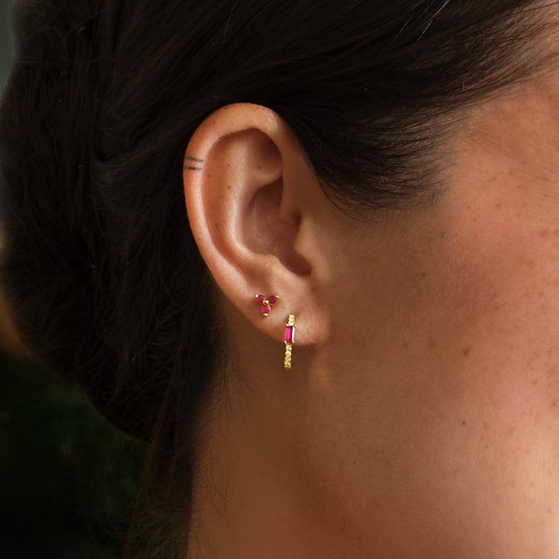 Ruby three-stone stud earring in 14kt yellow gold with three round red gems on ear.