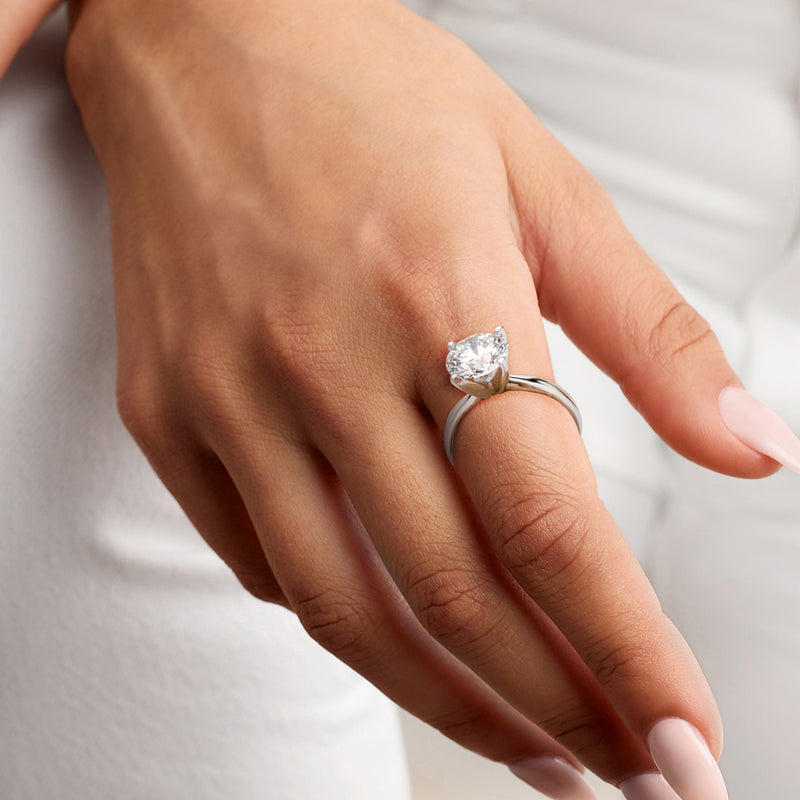 Platinum solitaire diamond ring on finger, round brilliant stone in four-prong mount.