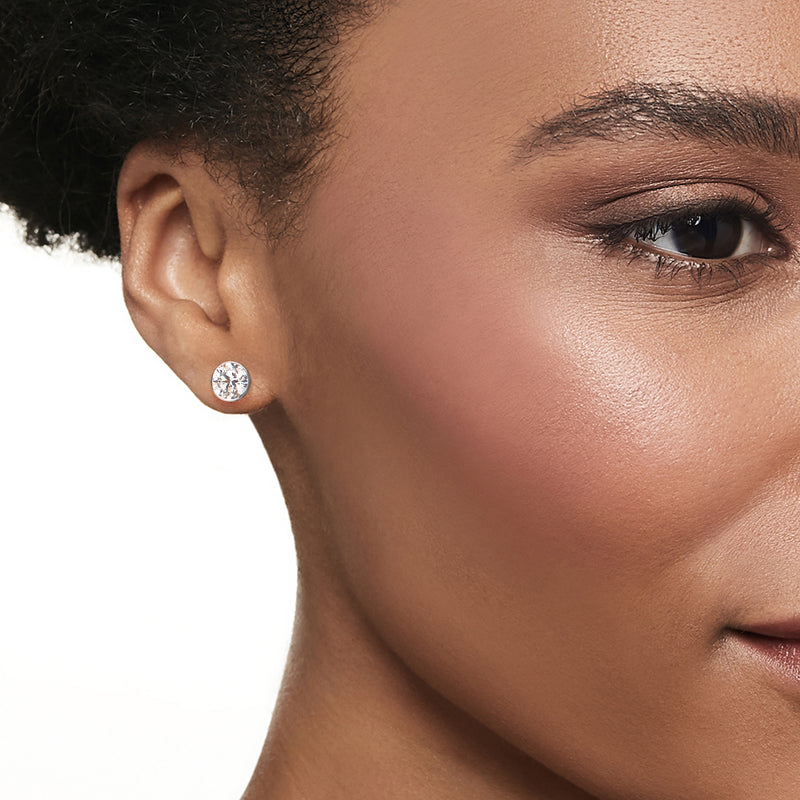 Round lab-grown diamond stud earrings in 14kt white gold, bezel set, on ear close-up.