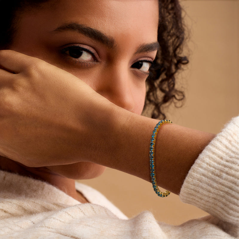 Blue gemstone tennis bracelet on wrist with gold links, clasp side visible