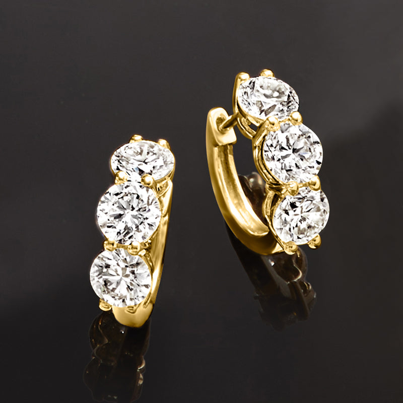 Yellow gold huggie hoop earrings with three round diamonds, angled close-up