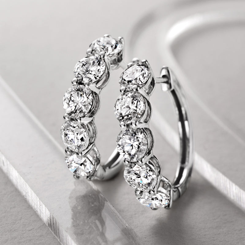 Five round diamond hoop earrings in white gold with bezel-set stones along the curve