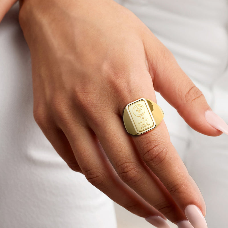Yellow gold signet ring on hand, square engraved face with fleur-de-lis mark.