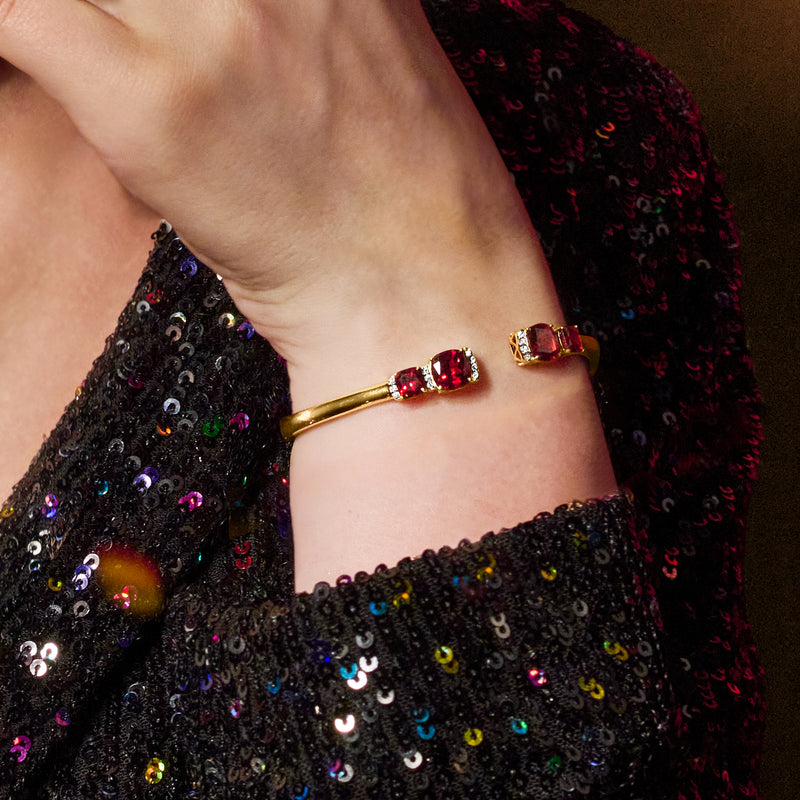 Gold cuff bracelet with red garnet stones and white topaz halo details on wrist