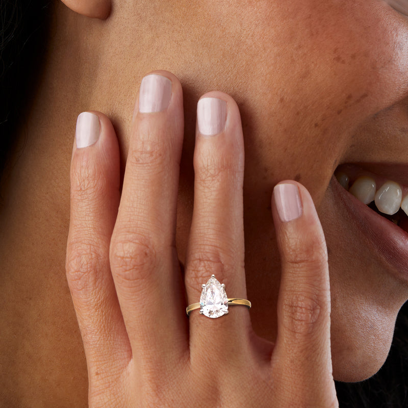Pear-cut diamond solitaire ring in 14kt yellow gold on finger, pear-shaped center stone